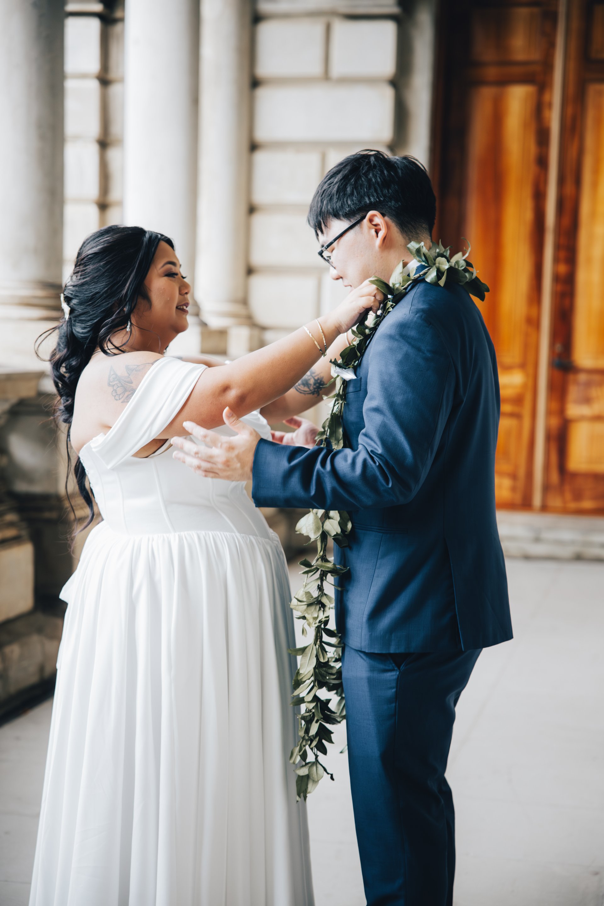 Bride places maile lei on groom during Hawaii wedding ceremony at historic venue